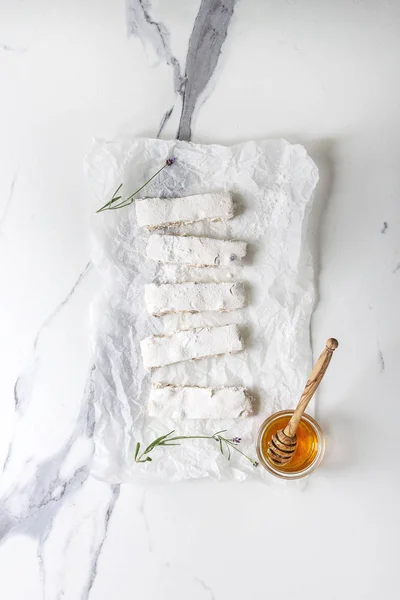 自家製蜂蜜ナッツ ヌガー Turron ラベンダー 白大理石の背景に蜂蜜と砂糖粉末ガラスと紙を丸めてでスライスされました フラット レイアウト — ストック写真