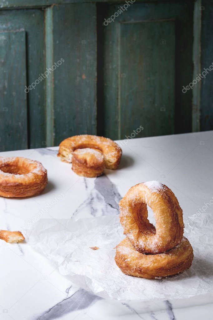 Homemade puff pastry deep fried donuts or cronuts with sugar standing on crumpled paper over white marble kitchen table.