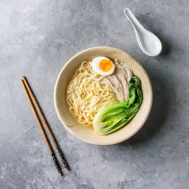 Asya yemek udon erişte ile haşlanmış yumurta, mantar, boc choy seramik kase kaşık ve yemek çubukları ile gri doku arka plan üzerinde servis. Üstten Görünüm, uzay.