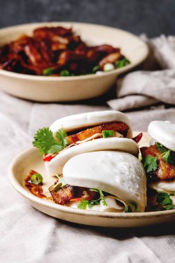 Asya sandviç Gua bao buns domuz eti, yeşil ve sebzeler ile keten masa örtüsü seramik tabak masaya servis ile atmak. Asya tarzı hızlı yiyecek yemek.