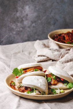 Asya sandviç Gua bao buns domuz eti, yeşil ve sebzeler ile keten masa örtüsü seramik tabak masaya servis ile atmak. Asya tarzı hızlı yiyecek yemek.