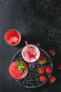 Üç farklı kırmızı meyve karpuz, çilek, ahududu, nar kokteyl veya smoothies içinde ezilmiş buz, taze nane, yukarıda malzemeler ile gözlük siyah arka plan üzerinde berry. Düz lay, uzay