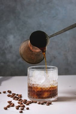 Cam vintage jezva ve arka plan, gri beton duvar ile beyaz mermer tabloda etrafında kahve çekirdekleri dökme kahve ile buzlu kahve kokteyl veya frappe buz küpleri ve krema ile servis.