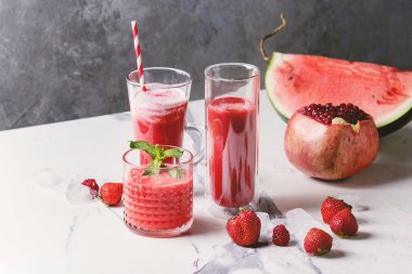 Üç farklı kırmızı meyve karpuz, çilek, ahududu, nar kokteyl veya ezilmiş buz, taze nane ve beyaz mermer tablo yukarıda malzemeler bardaklarda smoothies berry.