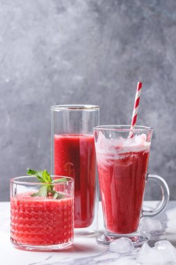 Üç farklı kırmızı meyve karpuz, çilek, ahududu, nar kokteyl veya ezilmiş buz, taze nane ve beyaz mermer tablo yukarıda malzemeler bardaklarda smoothies berry.