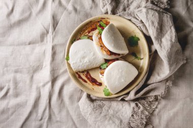 Asya sandviç Gua bao buns domuz eti, yeşil ve seramik tabak içinde keten masa örtüsü üzerinde hizmet sebze ile atmak. Asya tarzı hızlı yiyecek yemek. Düz lay, uzay