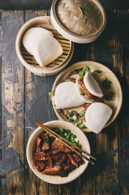 Asya sandviç Gua bao buns domuz eti, yeşil ve koyu ahşap tahta arka plan üzerinde seramik tabak içinde servis sebze ile atmak. Asya tarzı hızlı yiyecek yemek. Düz lay, uzay