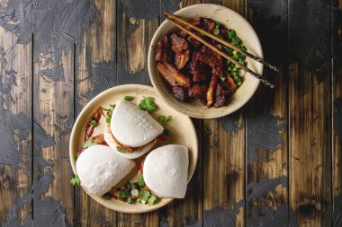 Asya sandviç Gua bao buns domuz eti, yeşil ve koyu ahşap tahta arka plan üzerinde seramik tabak içinde servis sebze ile atmak. Asya tarzı hızlı yiyecek yemek. Düz lay, uzay