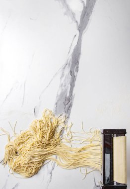 Ev yapımı İtalyan pişmemiş makarna spagetti makarna makine üreticisi ile İrmik unu beyaz mermer doku arka plan üzerinde rulo hamur. Düz lay, uzay.