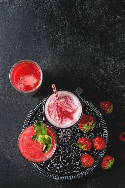 Üç farklı kırmızı meyve karpuz, çilek, ahududu, nar kokteyl veya smoothies içinde ezilmiş buz, taze nane, yukarıda malzemeler ile gözlük siyah arka plan üzerinde berry. Düz lay, uzay