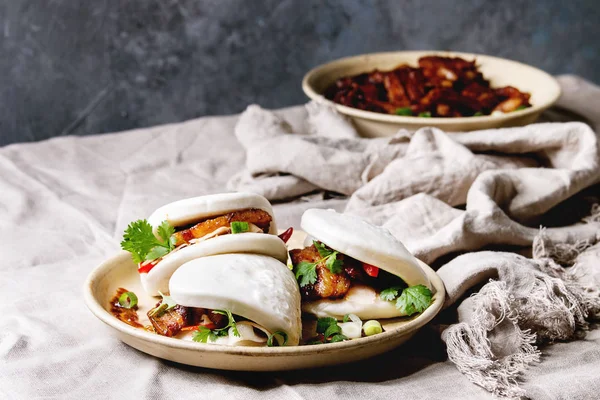 Asya sandviç Gua bao buns domuz eti, yeşil ve sebzeler ile keten masa örtüsü seramik tabak masaya servis ile atmak. Asya tarzı hızlı yiyecek yemek.