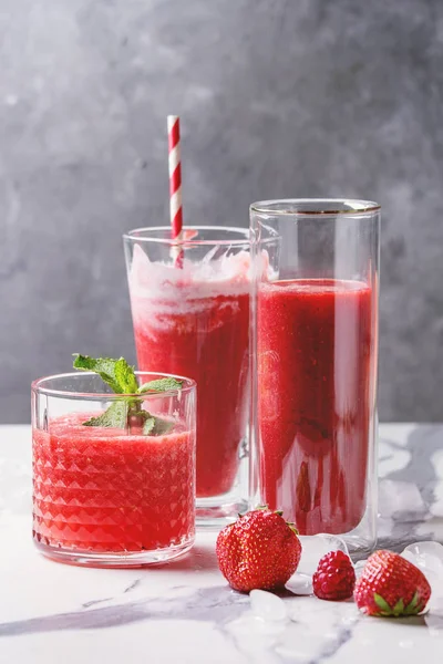 Üç farklı kırmızı meyve karpuz, çilek, ahududu, nar kokteyl veya ezilmiş buz, taze nane ve beyaz mermer tablo yukarıda malzemeler bardaklarda smoothies berry.