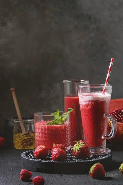 Üç farklı kırmızı meyve karpuz, çilek, ahududu, nar kokteyl veya ezilmiş buz, nane ve siyah doku tablo yukarıda malzemeler ile bardaklarda smoothies berry. Gıda natürmort.