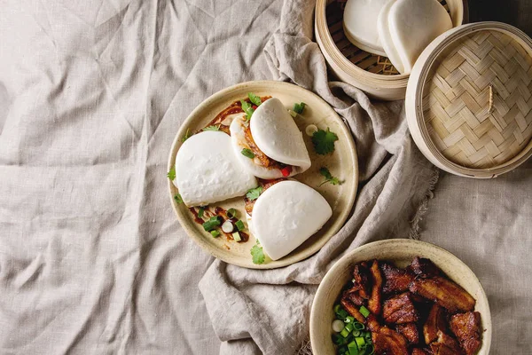 Asya sandviç Gua bao buns domuz eti, yeşil ve seramik tabak içinde keten masa örtüsü üzerinde hizmet sebze ile atmak. Asya tarzı hızlı yiyecek yemek. Düz lay, uzay