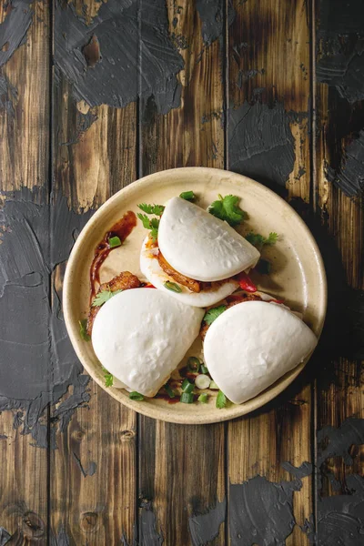 Asya sandviç Gua bao buns domuz eti, yeşil ve koyu ahşap tahta arka plan üzerinde seramik tabak içinde servis sebze ile atmak. Asya tarzı hızlı yiyecek yemek. Düz lay, uzay