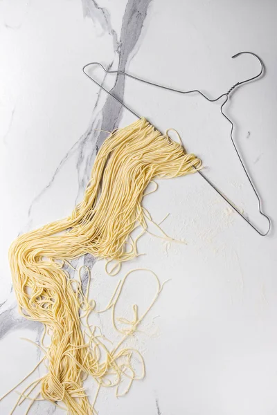 Ev yapımı İtalyan pişmemiş makarna spagetti beyaz mermer doku arka plan üzerinde elbise askısı üzerinde kurumuş. Düz lay, uzay.