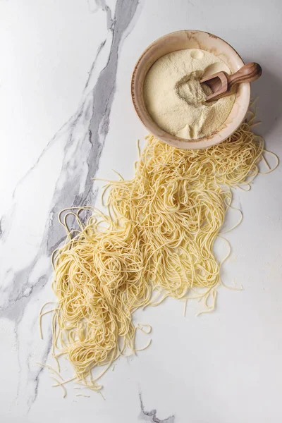 Ev yapımı İtalyan pişmemiş makarna İrmik unu beyaz mermer doku arka plan üzerinde kâse spagetti. Düz lay, uzay.