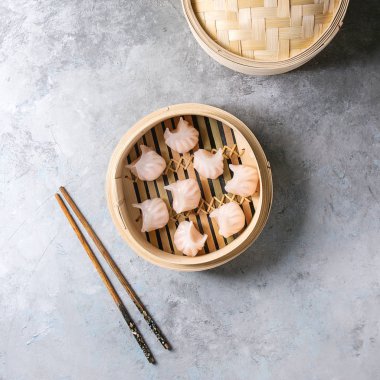 Asya Buhar potstickers köfte tarafından açılan bambu vapur karides gri doku arka plan üzerinde yemek çubukları ile doldurulmuş. Üstten görünüm alanı. Kare görüntü