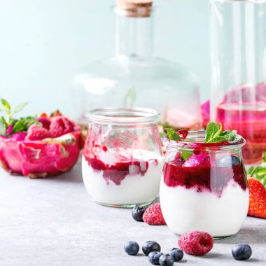 Berry soslu beyaz doğal yoğurt, meyve salatası pembe dragon meyve, çilek ve nane, kavanoz limonata gri masada şişe ile servis. Sağlıklı beslenme. Uzay kopyalayın. Kare görüntü