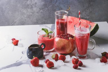 Üç farklı kırmızı meyve karpuz, çilek, ahududu, nar kokteyl veya ezilmiş buz, taze nane ve beyaz mermer tablo yukarıda malzemeler bardaklarda smoothies berry.
