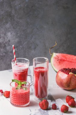 Üç farklı kırmızı meyve karpuz, çilek, ahududu, nar kokteyl veya ezilmiş buz, taze nane ve beyaz mermer tablo yukarıda malzemeler bardaklarda smoothies berry.
