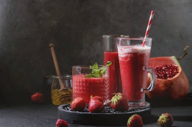 Üç farklı kırmızı meyve karpuz, çilek, ahududu, nar kokteyl veya ezilmiş buz, nane ve siyah doku tablo yukarıda malzemeler ile bardaklarda smoothies berry. Gıda natürmort.