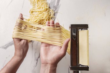 Rulo hamur için ev yapımı İtalyan pişmemiş makarna spagetti makarna makine üreticisi ile İrmik unu beyaz mermer doku arka plan üzerinde elinde. Düz lay, uzay.