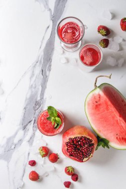 Üç farklı kırmızı meyve karpuz, çilek, ahududu, nar kokteyl veya ezilmiş buz, taze nane, yukarıda malzemeler ile bardaklarda smoothies beyaz mermer arka plan üzerinde berry. Düz yatıyordu