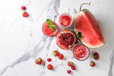 Üç farklı kırmızı meyve karpuz, çilek, ahududu, nar kokteyl veya ezilmiş buz, taze nane, yukarıda malzemeler ile bardaklarda smoothies beyaz mermer arka plan üzerinde berry. Düz yatıyordu