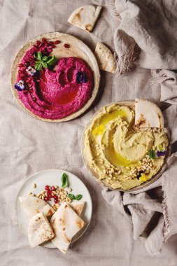 Ev yapımı geleneksel ve pancar yayılmış humus çam fıstığı, zeytinyağı, nar ile çeşitli Seramik tabaklar keten kumaş arka plan üzerinde pide ekmek ve yeşil salata ile servis. Düz lay, uzay.