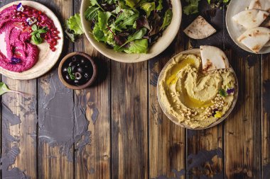 Ev yapımı geleneksel ve pancar yayılmış humus çam fıstığı, zeytinyağı, nar ile çeşitli Seramik tabaklar koyu ahşap arka plan üzerinde pide ekmek ve yeşil salata ile servis. Düz lay, uzay.