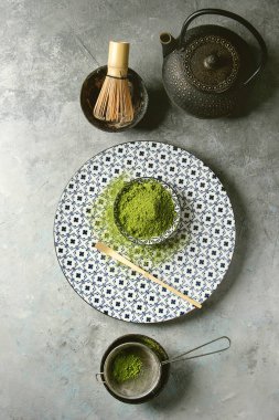 Matcha içecek yapmak için malzemeler. Yeşil çay matcha tozu seramik kase, geleneksel bambu kaşık ve fırçalamak dekoratif kaplama, siyah demir demlik gri doku arka plan üzerinde üzerinde. Düz lay, uzay