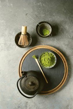 Matcha içecek yapmak için malzemeler. Yeşil çay matcha tozu seramik kase, geleneksel bambu kaşık ve fırçalamak kayrak kurulu, siyah demir demlik gri doku arka plan üzerinde üzerinde. Düz lay, uzay