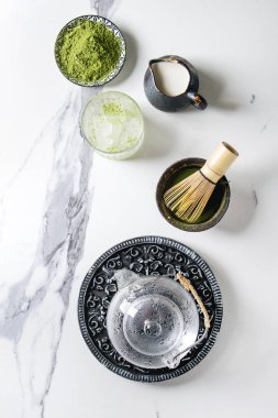 İçki matcha buz yapmak için malzemeler. Yeşil çay matcha tozu seramik kase, geleneksel bambu kaşık, çırpma teli, süt, cam Çaydanlık, buz küpleri üzerinden beyaz mermer zemin. Düz lay, uzay