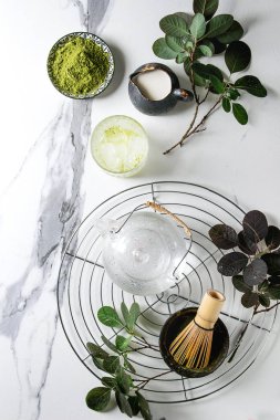 İçki matcha buz yapmak için malzemeler. Yeşil çay matcha tozu seramik kase, geleneksel bambu kaşık, çırpma teli üzerinde soğutma raf, cam Çaydanlık, buz küpleri beyaz mermer zemin. Düz lay, uzay