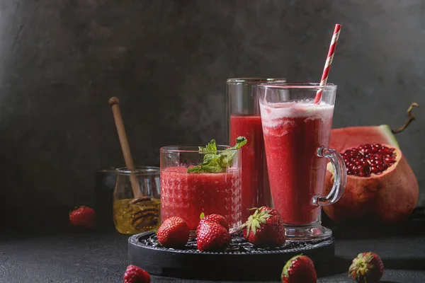 Üç farklı kırmızı meyve karpuz, çilek, ahududu, nar kokteyl veya ezilmiş buz, nane ve siyah doku tablo yukarıda malzemeler ile bardaklarda smoothies berry. Gıda natürmort.