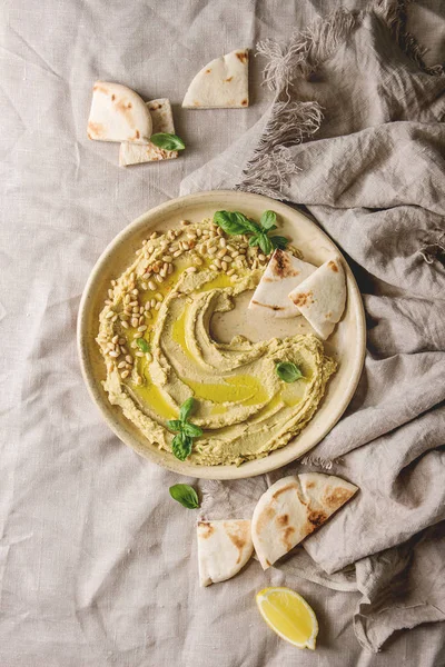 Ev yapımı geleneksel yayılmış humus çam fıstığı, zeytin yağı, fesleğen ile keten kumaş arka plan üzerinde seramik tabak Pide ile servis. Düz lay, alan. Akdeniz snack.