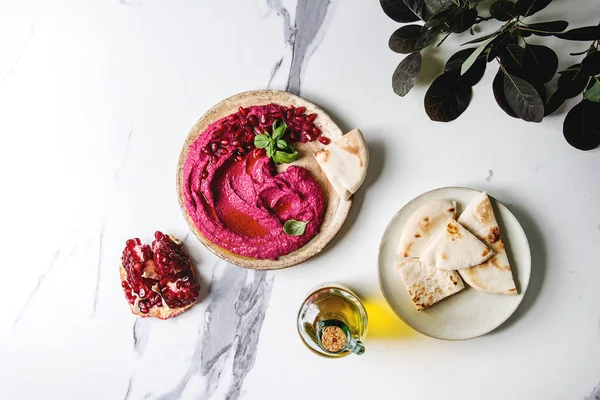 Ev yapımı yayılan kırmızı pancar humus nar taneleri, zeytin yağı, fesleğen ile beyaz mermer arka plan üzerinde pide ekmek ve yeşil Şubesi ile seramik plaka üzerinde görev yaptı. Düz lay, alan. Akdeniz snack.