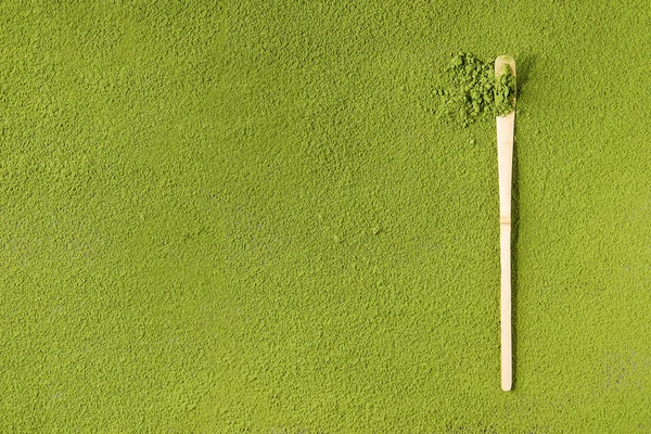 Green tea matcha powder in traditional bamboo spoon over powdering matcha as background.