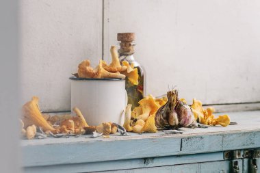 Mavi Beyaz ahşap mutfak masasında şişe zeytinyağı ve sarımsak ile beyaz emaye mug içinde çiğ çiğ Chanterelles orman mantar. Rustik tarzı, gün ışığı, kopya alanı