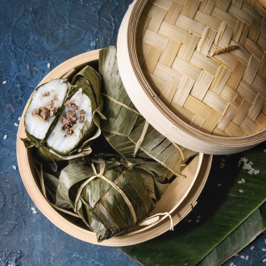 Asya pirinç piramidal pirinç tapyoka un dan Köfte Buğulama, muz doldurma et bambu gemi pilav ile mavi doku arka plan üzerinde hizmet bırakır. Üstten görünüm alanı. Kare görüntü