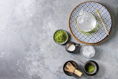 İçki matcha buz yapmak için malzemeler. Yeşil çay matcha tozu seramik kase, geleneksel bambu kaşık, plaka, cam Çaydanlık, çırpma teli buz küpleri gri doku arka plan üzerinde. Düz lay, uzay