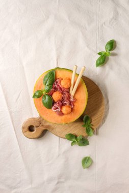 Kavun ve jambon ya da jambon salata kavun karpuz yarısını servis, taze fesleğen ve ahşap hizmet kurulu grisini ekmek kadeh beyaz şarap ile beyaz keten kumaş üzerine dekore edilmiştir. Düz lay, uzay