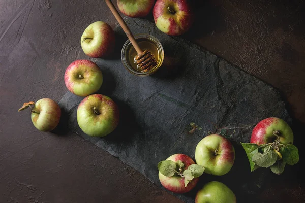 Olgun organik bahçe yeşil kırmızı elma ile yaprakları ve kavanoz bal karanlık doku arka plan üzerinde siyah arduvaz gemide. Düz lay, alan. Sonbaharda hasat.