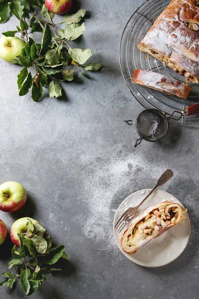 スライスした自家製のパイ生地のアップルパイ シュトルーデル ラックの冷却に灰色のテクスチャ背景に熟した新鮮なリンゴ フォークと砂糖粉を添えてください フラット レイアウト — ストック写真