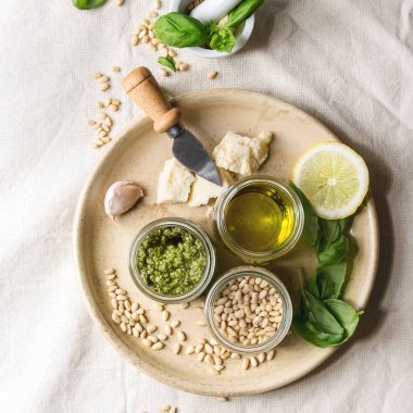 Geleneksel fesleğen pesto sos cam. Malzemeler taze fesleğen, zeytinyağı, parmesan peyniri, çam fıstığı, limon beyaz keten kumaş arka plan üzerinde seramik plaka üzerinde yukarıda. Üstten görünüm alanı. Kare görüntü
