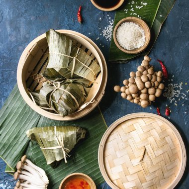 Bambu gemi içinde hizmet muz yaprakları doldurma etli köfte pirinç tapyoka un dan Asya pirinç piramidal biraz uzun tuttum. Malzemeler, soslar yukarıda. Mavi doku arka plan. Üstten görünüm. Kare görüntü