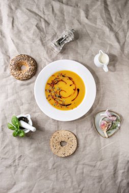 Vejetaryen Kabak havuç çorbası tabak arka plan olarak keten kumaş üzerinde yukarıda sarımsak otlar, kaşık, kabı krem, Simit Ekmek, kara biber, balsamik sirke tarafından dekore edilmiş. Düz lay, uzay
