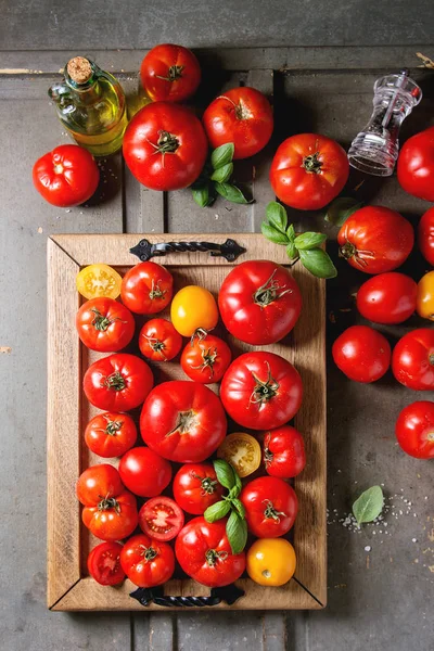 各种成熟的新鲜有机园艺西红柿不同种类和颜色与水斑点 罗勒叶子在托盘瓶橄榄油 胡椒和盐老灰色木背景 — 图库照片