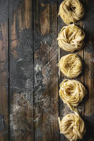 各种意大利自制的生肉面食和面条与粉面粉在深色木板纹理木桌 复制空间 — 图库照片